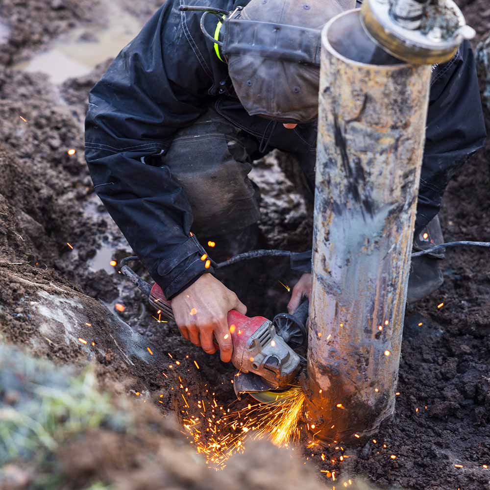 Person som svetsar ihop ett rör i marken